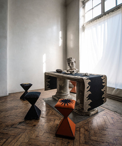 Marble pedestal console table with black and tan flame bordered runner with a bust, framed by sculptural side stools.