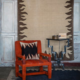 Red leather chair set against a Handknotted rug with a flame border design in brown on a cream field.