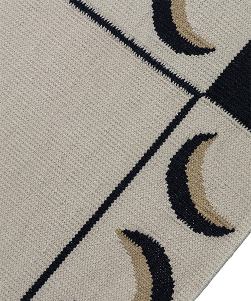 Detail of a flatweave rug with a crescent moon border in cream, taupe and black.
