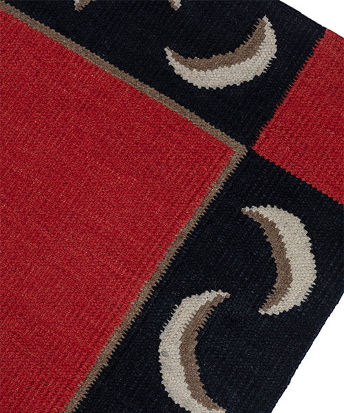Detail of a flatweave runner with a crescent moon border in cream, taupe and black of a red field.