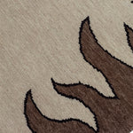 Detail of a handknotted rug with a flame border design in brown on a cream field.