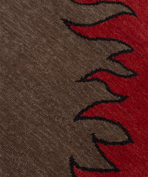 Detail of a handknotted rug with a flame border design in red on a brown field. 