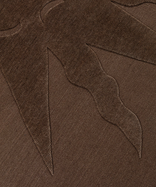 Detail of a handknotted rug with a raised sun motif in tonal brown.