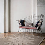 Wire bench with flame motif throw pillows atop a handknotted rug with a raised sun motif in tonal brown