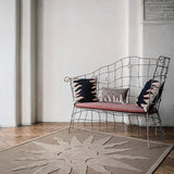 Wire bench with flame motif throw pillows atop a handknotted rug with a raised sun motif in tonal brown