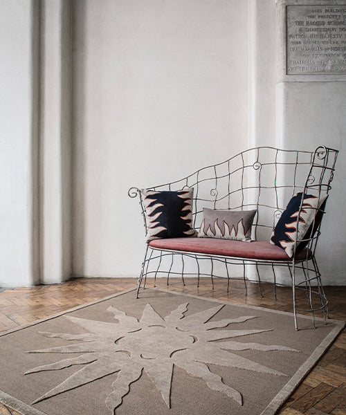 Wire bench with flame motif throw pillows atop a handknotted rug with a raised sun motif in tonal brown