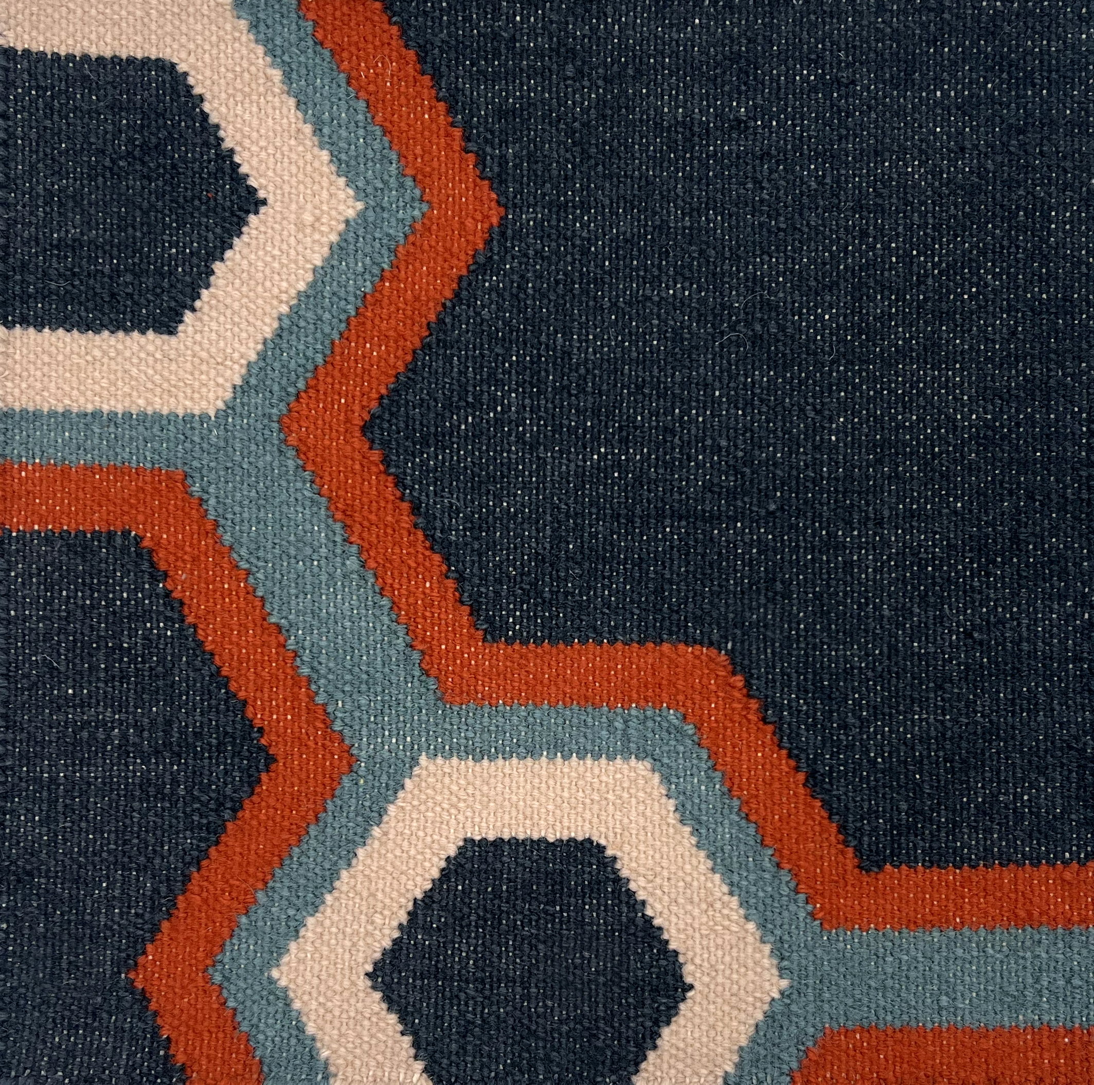 Detail of a flatwoven rug in a bold geometric floral-like design in blue, navy, red and cream. 