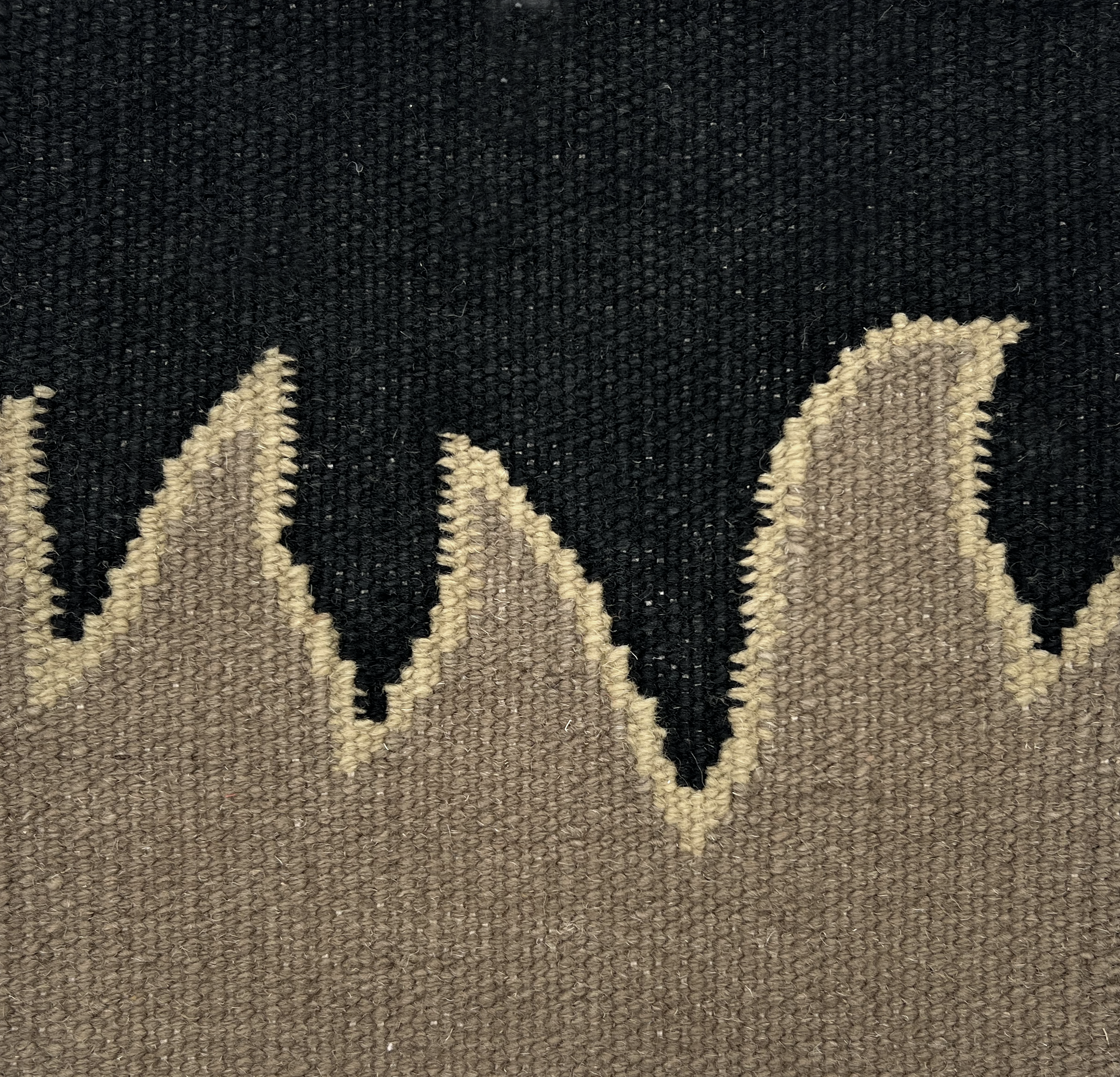 Detail of a flatweave rug with a flame border design in taupe on a black