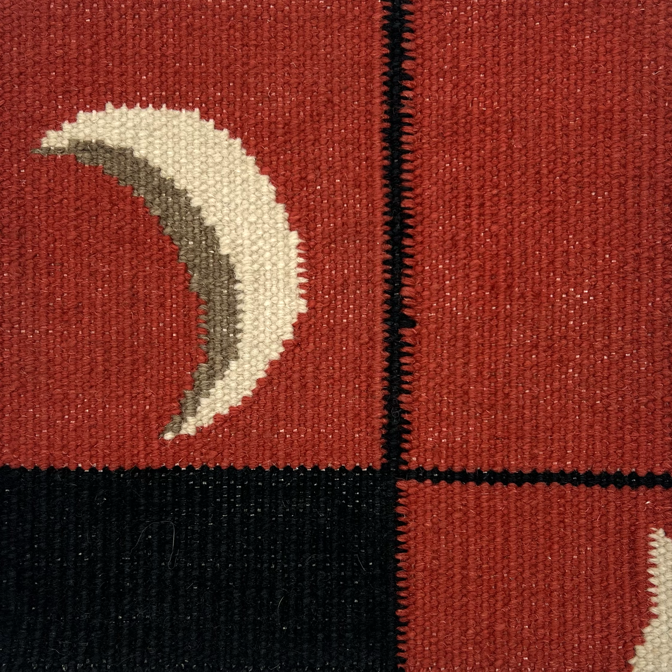 Detail of a flatweave runner with a crescent moon border in cream, taupe and black of a red field.