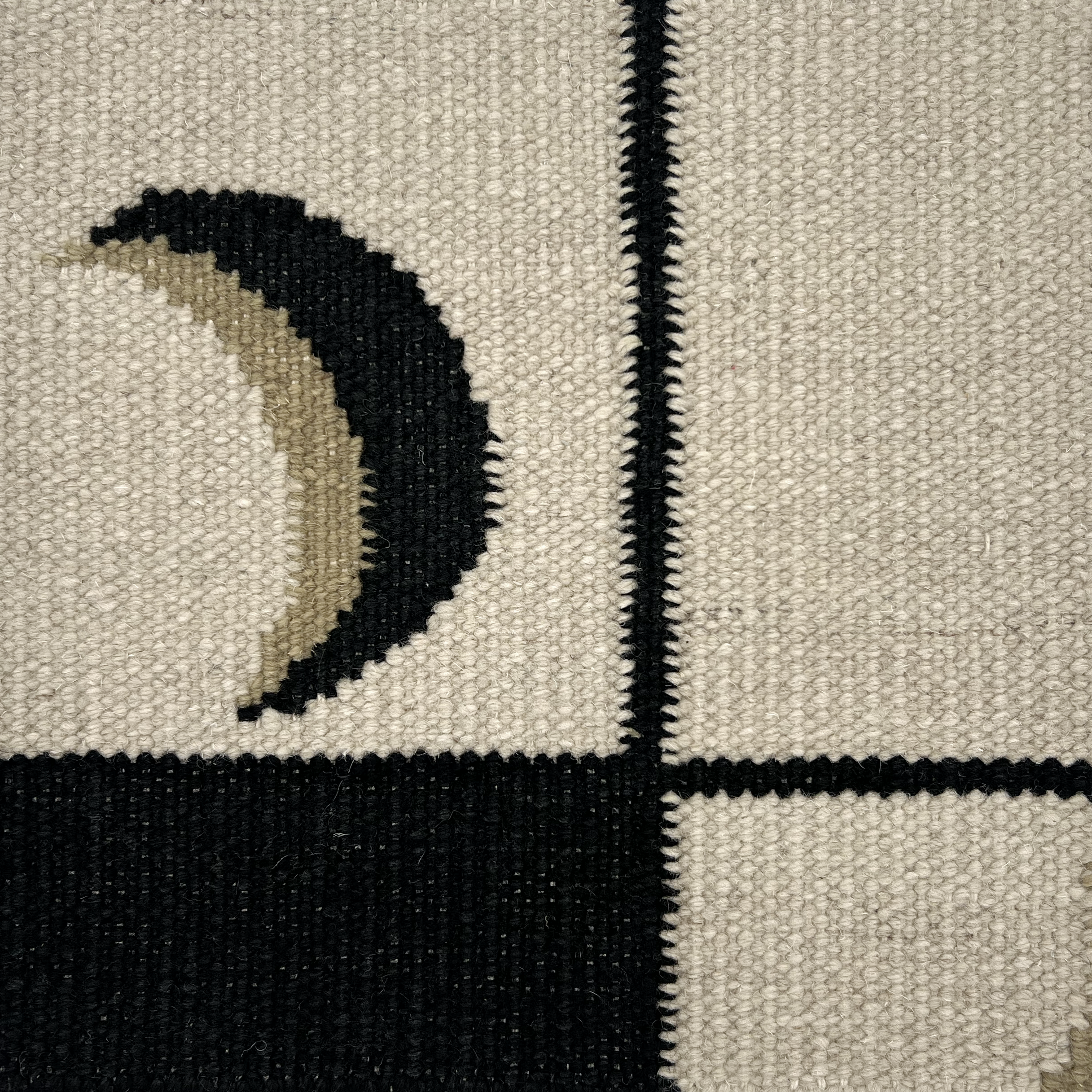 Detail of a flatweave rug with a crescent moon border in cream, taupe and black.