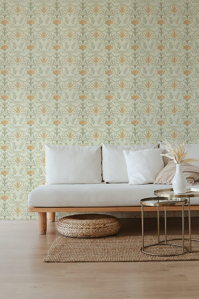 A couch and wooden end table stand in front of a wall papered in an intricate floral lattice print in green, orange and cream.