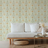 A couch and wooden end table stand in front of a wall papered in an intricate floral lattice print in green, orange and cream.