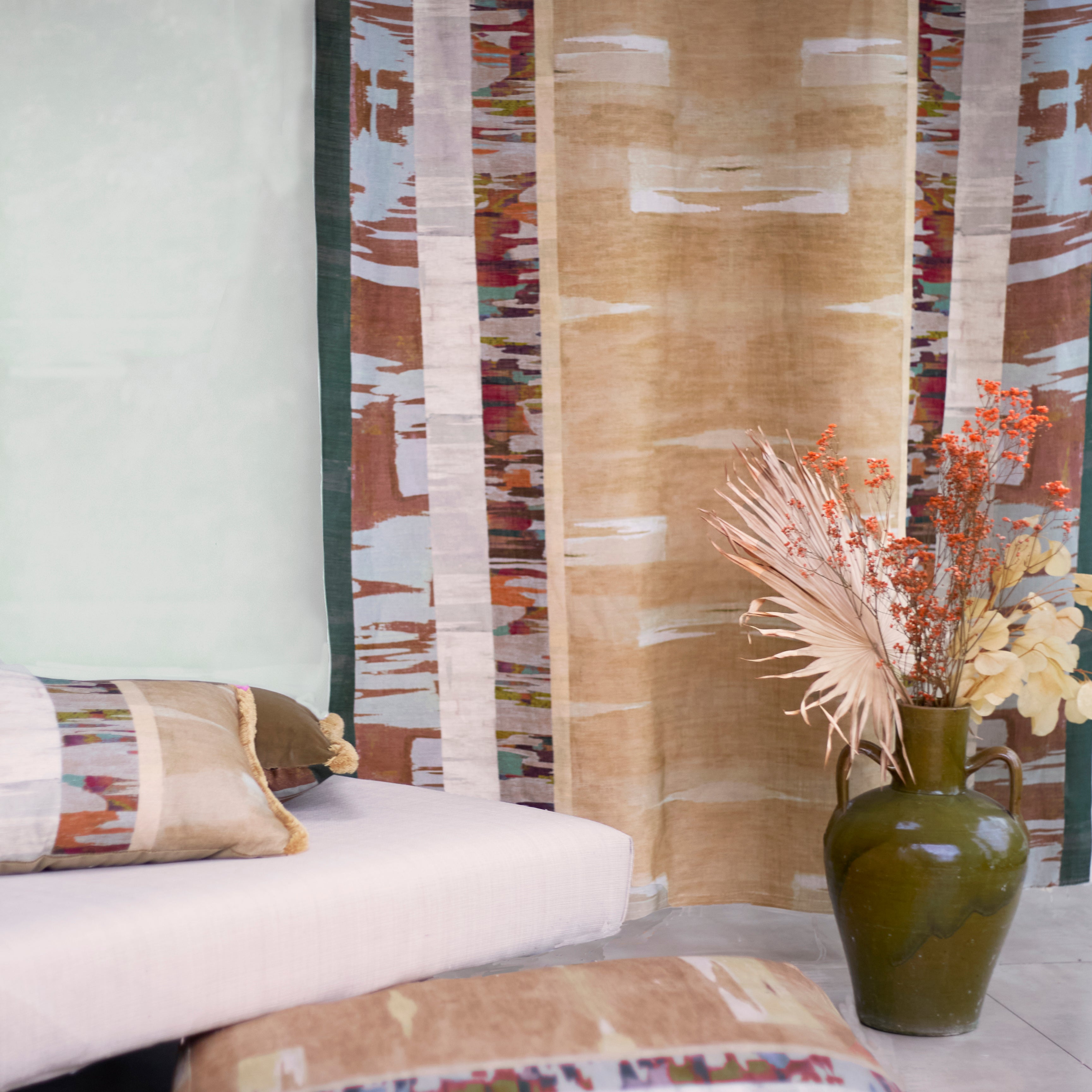 Living room scene, floor cushion, throw pillow and printed panel in a graphic watercolor stripe with ceramic urn with flowers and a white upholstered setee.