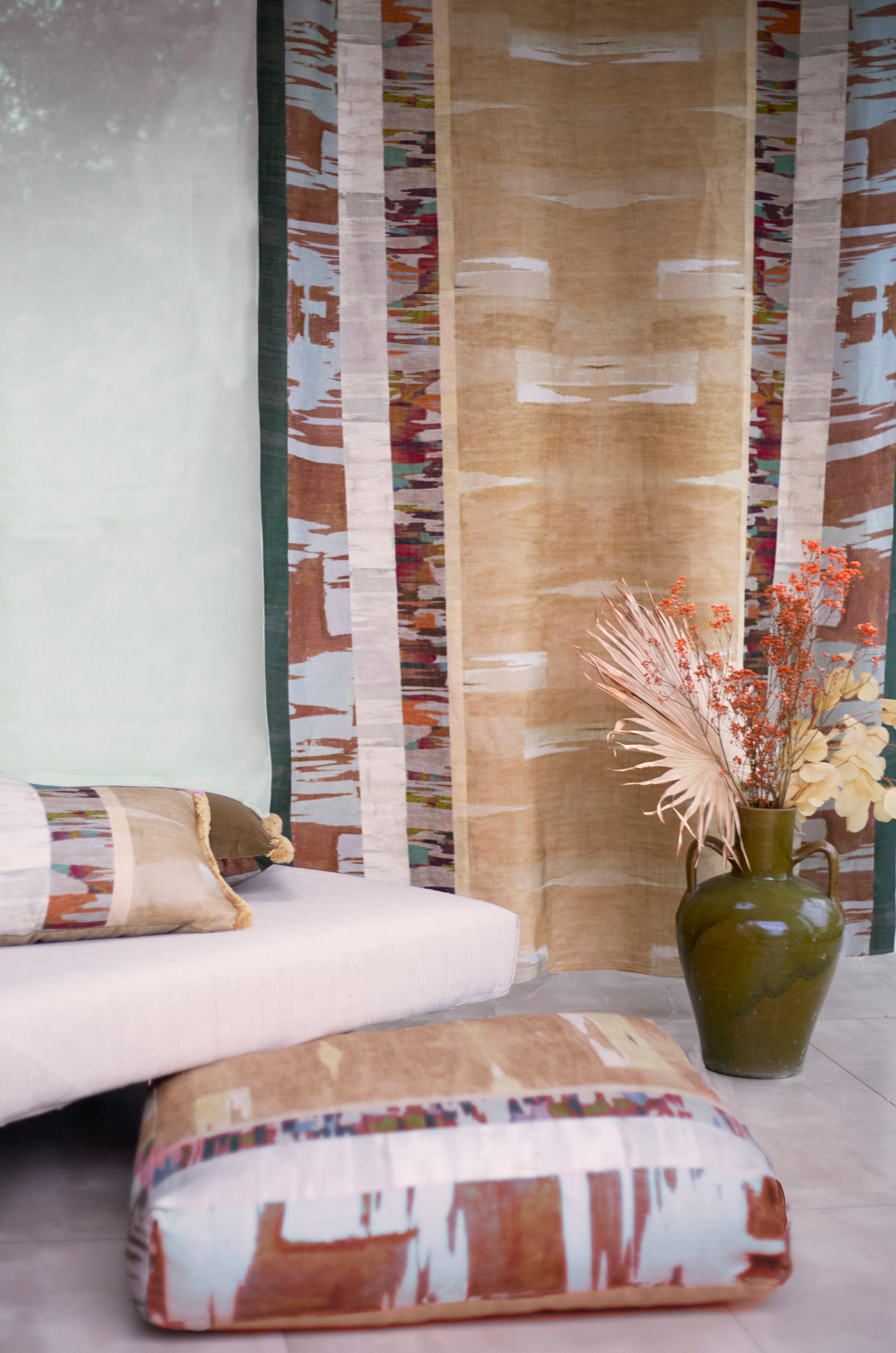 Living room scene, floor cushion, throw pillow and printed panel in a graphic watercolor stripe with ceramic urn with flowers and a white upholstered setee.