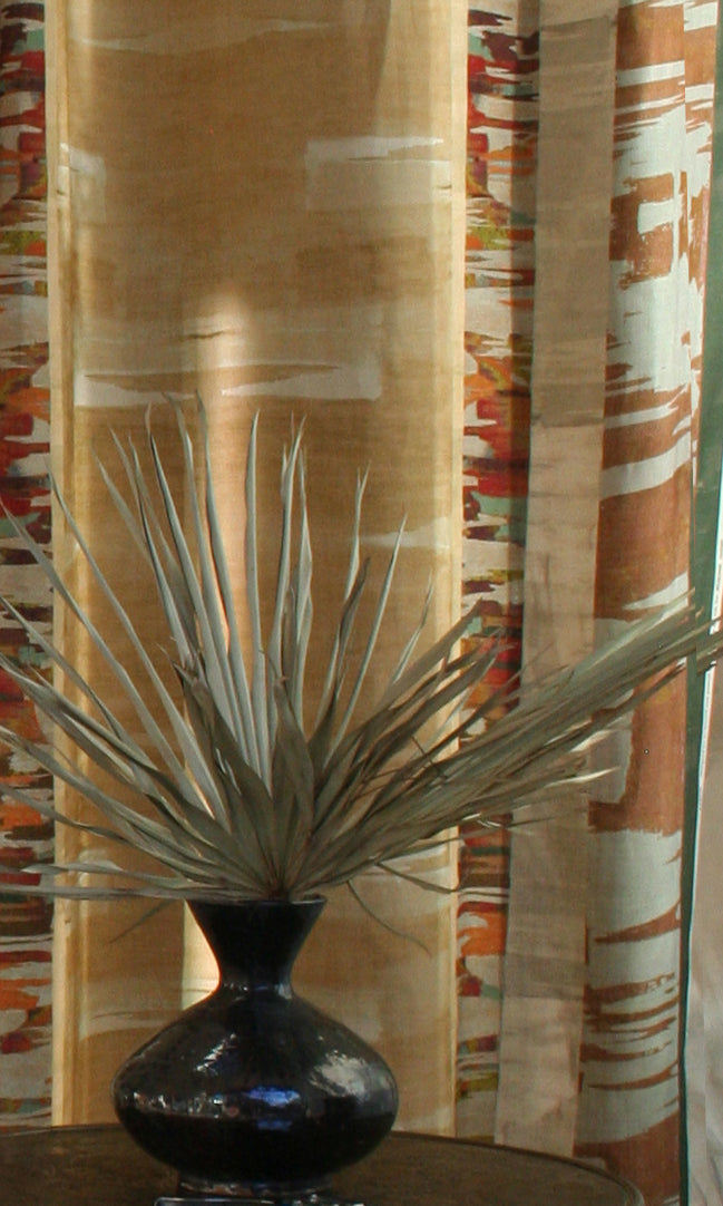 Printed fabric in an engineered stripe design with watercolor effects in shades of turquoise, beige and brown with a black vase and palm fronds.
