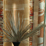 Printed fabric in an engineered stripe design with watercolor effects in shades of turquoise, beige and brown with a black vase and palm fronds.