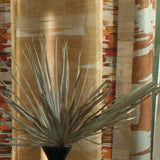 Printed fabric in an engineered stripe design with watercolor effects in shades of turquoise, beige and brown with a black vase and palm fronds.