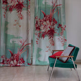 Two curtain panels in a watercolor mural in red and tuquoise with a side chair and throw pillows