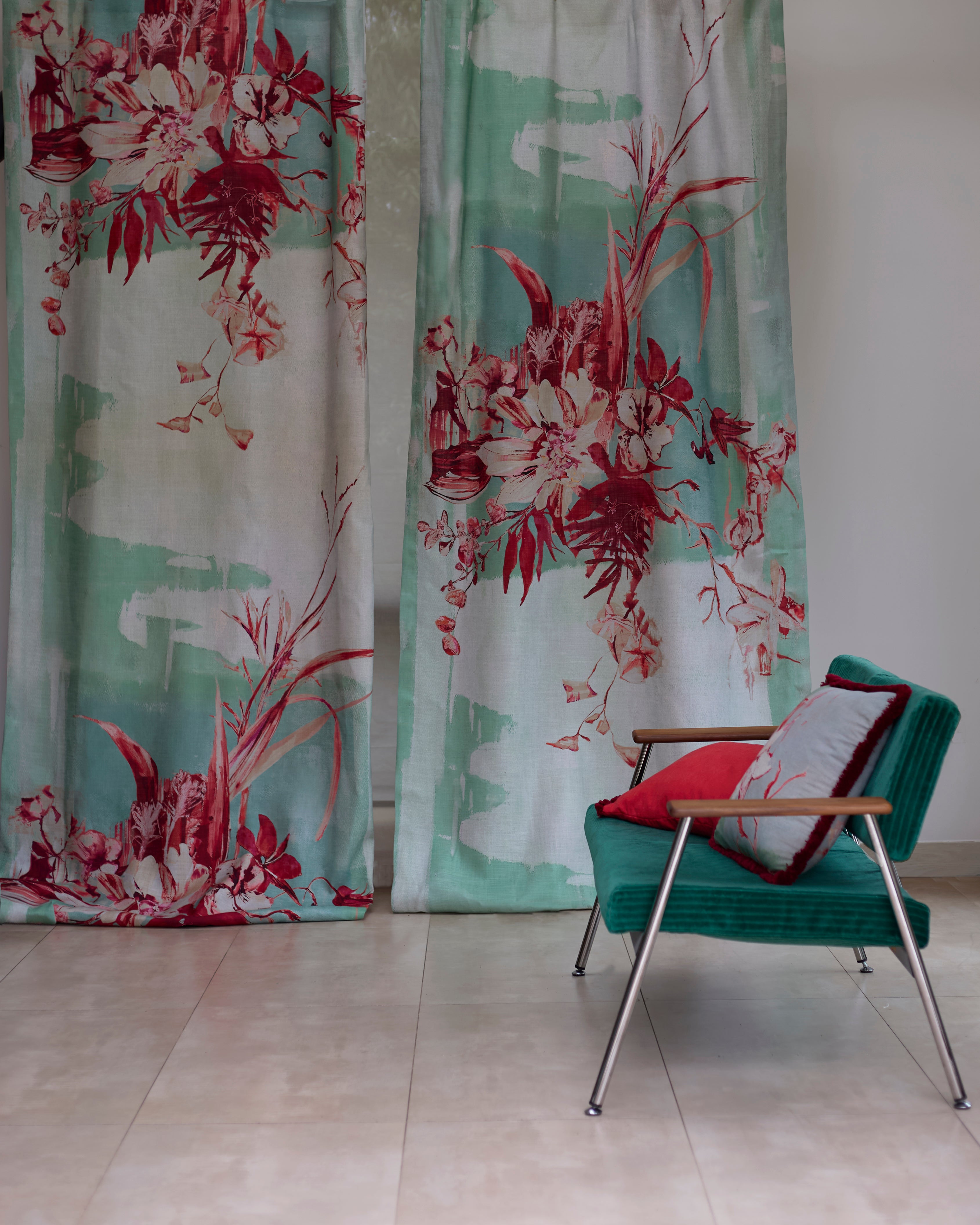 Two curtain panels in a watercolor mural in red and tuquoise with a side chair and throw pillows