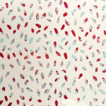 A vase of flowers stands in front of a wall covered in a playful paint blotch print in red and blue on a cream field.