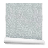 A hanging roll of wallpaper with a large-scale repeating leaf print in white on a blue-gray watercolor background.