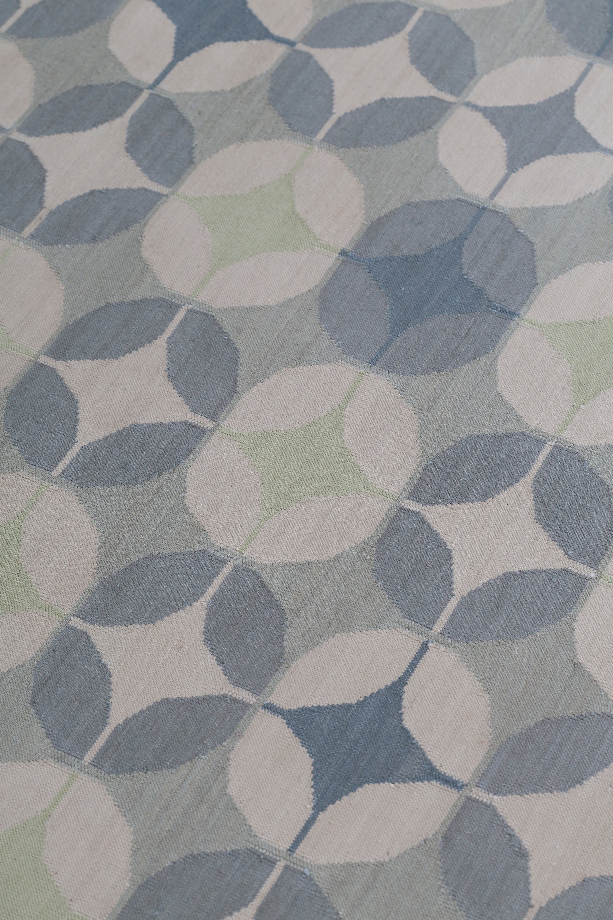 Detail of Alhambra Rug in Seafret featuring pattern of linked circles that create a star like lattice in a range of pale blues, with a light green accent on a soft white field. 