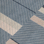 Detail of the Amelia Rug in Lapiz featuring a minimalist broken stripe pattern, overlayed with thin light blue diagonal lines. The broken stripes are a mix of navy blue, pale blue. white and turquoise with black accents, all on denim blue field.