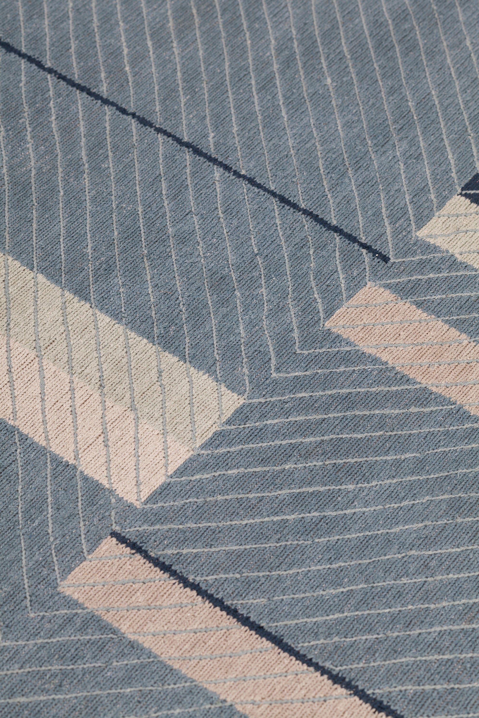 Detail of the Amelia Rug in Lapiz featuring a minimalist broken stripe pattern, overlayed with thin light blue diagonal lines. The broken stripes are a mix of navy blue, pale blue. white and turquoise with black accents, all on denim blue field.