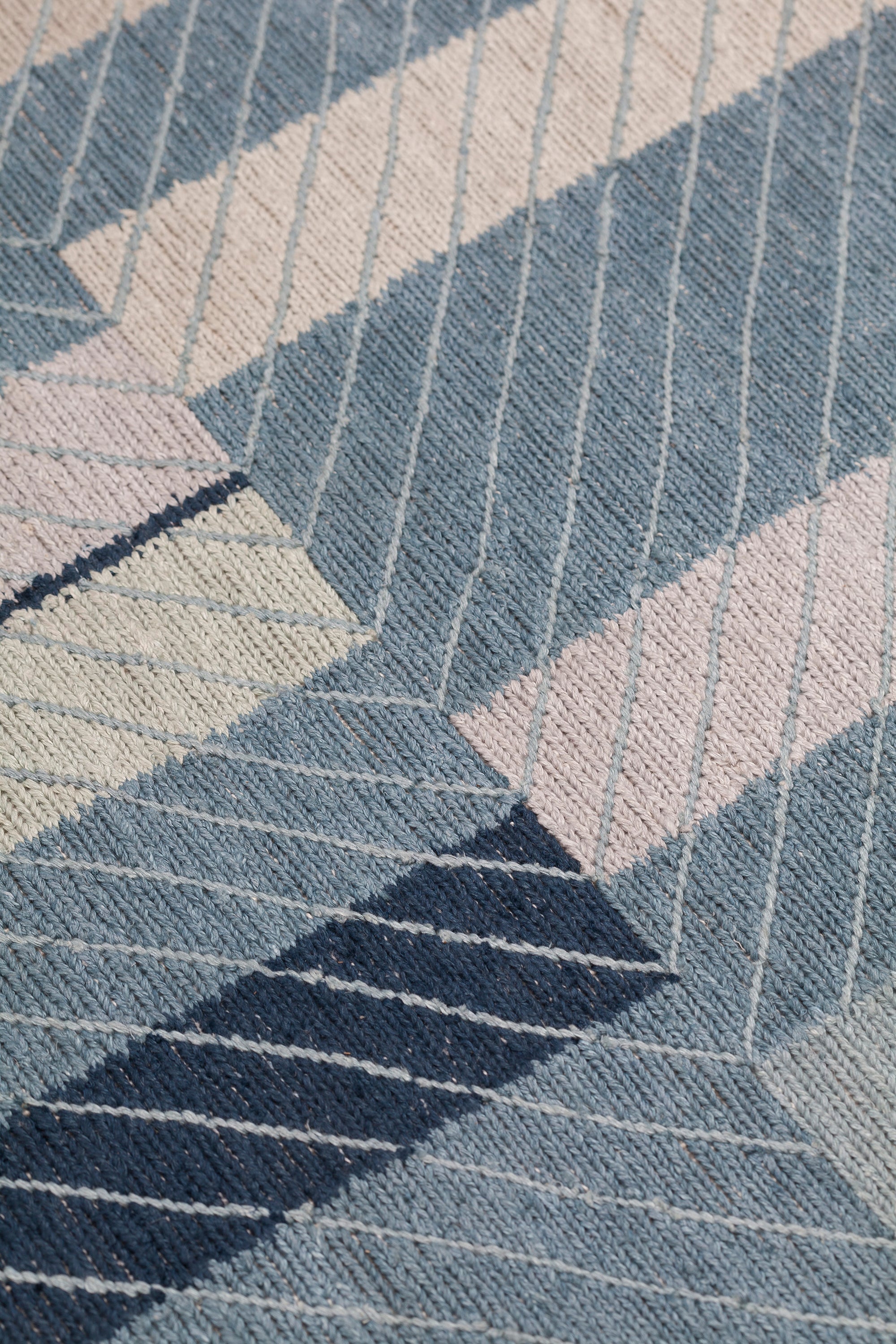 Detail of the Amelia Rug in Lapiz featuring a minimalist broken stripe pattern, overlayed with thin light blue diagonal lines. The broken stripes are a mix of navy blue, pale blue. white and turquoise with black accents, all on denim blue field.