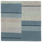 Detail of the Amelia Rug in Lapiz featuring a minimalist broken stripe pattern, overlayed with thin light blue diagonal lines. The broken stripes are a mix of navy blue, pale blue. white and turquoise with black accents, all on denim blue field.