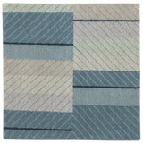 Detail of the Amelia Rug in Lapiz featuring a minimalist broken stripe pattern, overlayed with thin light blue diagonal lines. The broken stripes are a mix of navy blue, pale blue. white and turquoise with black accents, all on denim blue field.