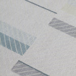 Detail of the Amelia Rug in Pearl featuring a minimalist broken stripe pattern, overlayed with thin white diagonal lines. The broken stripes are a mix of pale blues, grey, and turquoise with slate grey accents, all on a pale grey field. 