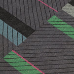 Detail of the Amelia Rug in Spinel featuring a minimalist broken stripe pattern, overlayed with thin black diagonal lines. The broken stripes are a mix of white, grey, kelly green, denim blue, black with hot pink accents, all on a charcoal grey field. 