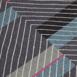 Detail of the Amelia Rug in Spinel featuring a minimalist broken stripe pattern, overlayed with thin black diagonal lines. The broken stripes are a mix of white, grey, kelly green, denim blue, black with hot pink accents, all on a charcoal grey field. 