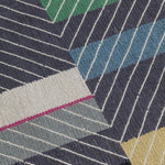 Detail of the Amelia Rug in Spinel featuring a minimalist broken stripe pattern, overlayed with thin black diagonal lines. The broken stripes are a mix of white, grey, kelly green, denim blue, black with hot pink accents, all on a charcoal grey field. 