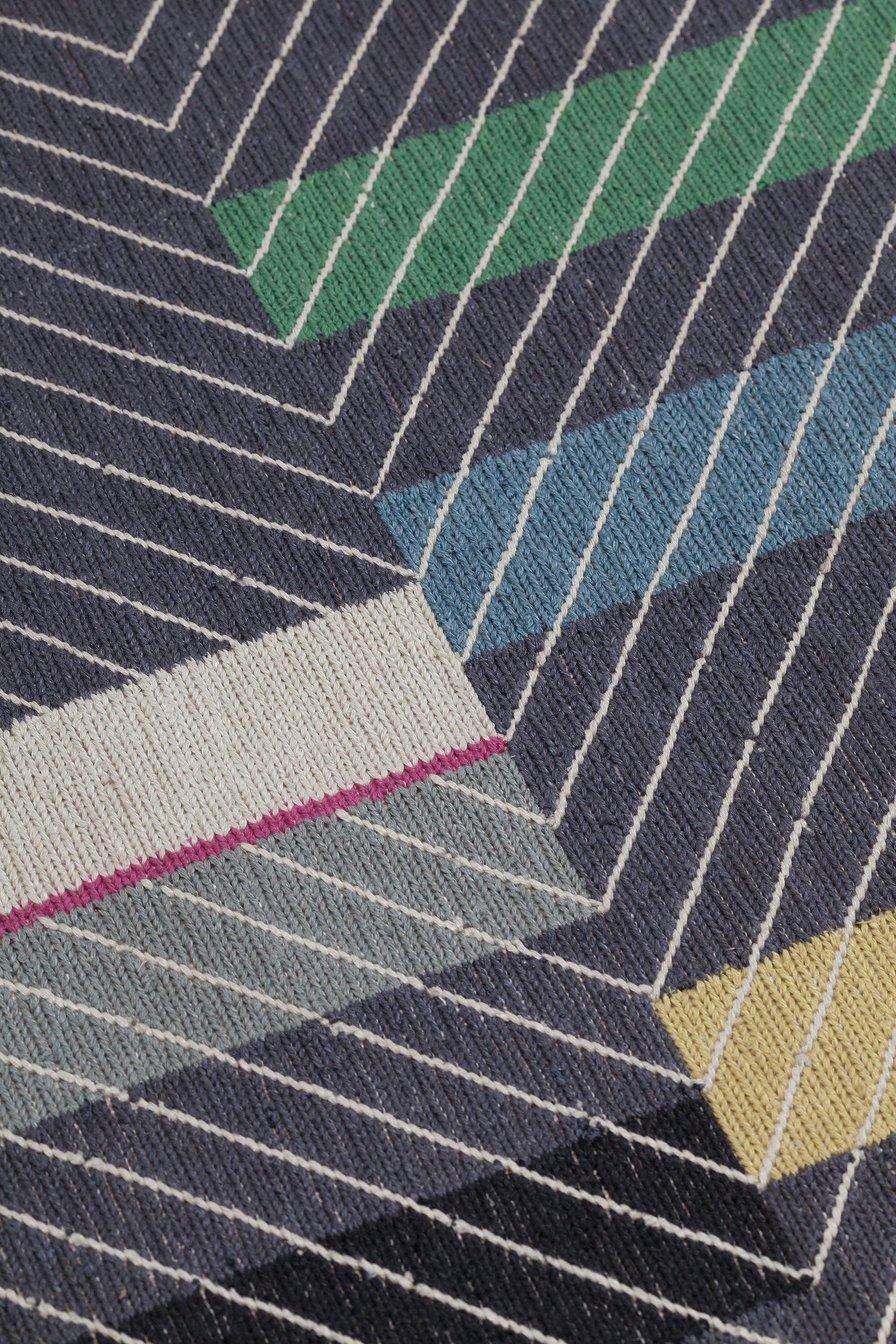 Detail of the Amelia Rug in Spinel featuring a minimalist broken stripe pattern, overlayed with thin black diagonal lines. The broken stripes are a mix of white, grey, kelly green, denim blue, black with hot pink accents, all on a charcoal grey field. 