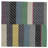 Detail of the Amelia Rug in Spinel featuring a minimalist broken stripe pattern, overlayed with thin black diagonal lines. The broken stripes are a mix of white, grey, kelly green, denim blue, black with hot pink accents, all on a charcoal grey field. 