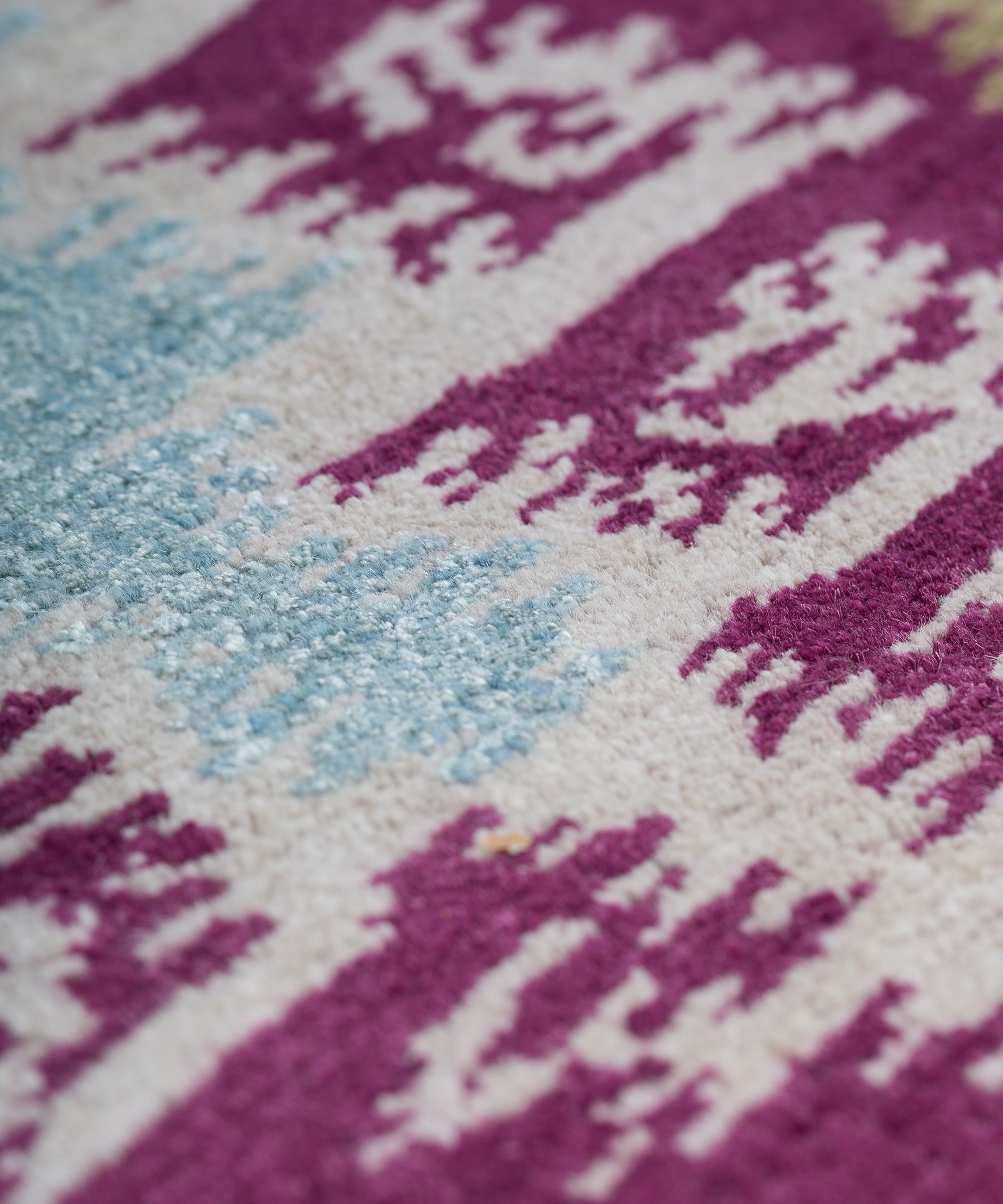 Detail of the Anna Ikat rug in Cranberry features an ikat inspired pattern of diamonds in blue and white with pale lime green accents on a magenta field