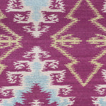 Detail of the Anna Ikat rug in Cranberry features an ikat inspired pattern of diamonds in blue and white with pale lime green accents on a magenta field