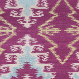 Detail of the Anna Ikat rug in Cranberry features an ikat inspired pattern of diamonds in blue and white with pale lime green accents on a magenta field
