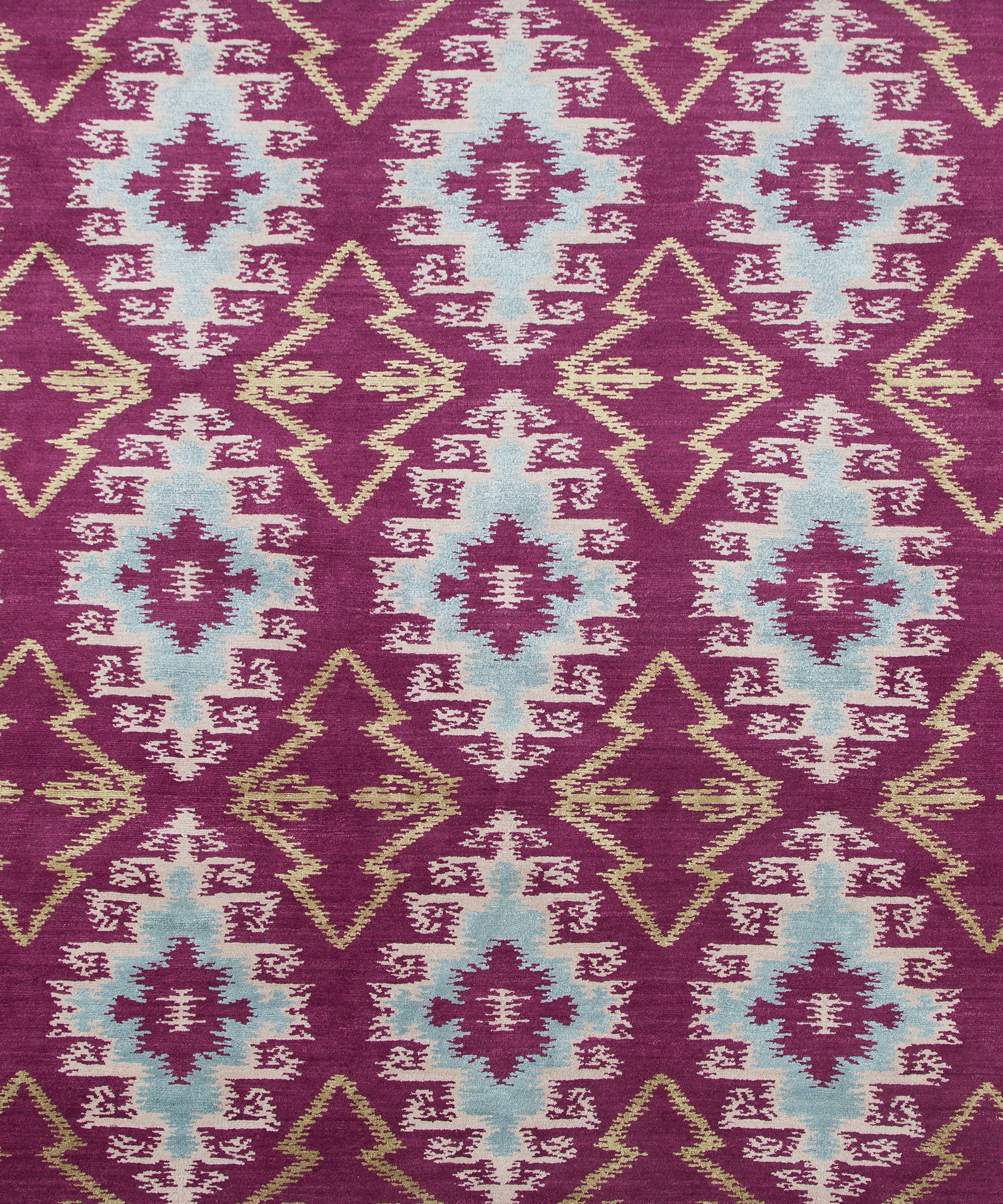 Full Size Anna Ikat rug in Cranberry features an ikat inspired pattern of diamonds in blue and white with pale lime green accents on a magenta field