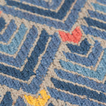 Detail of the Arrow Rug in Indigo-Coral features a dense pattern of nesting arrow shapes in shades of blue with accents of coral and yellow on a light brown field