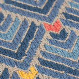 Detail of the Arrow Rug in Indigo-Coral features a dense pattern of nesting arrow shapes in shades of blue with accents of coral and yellow on a light brown field
