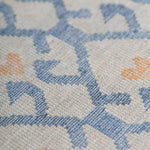 Detail of the Avesta Rug in Blue, a blue lattice pattern on a beige field with small orange heart accents. 