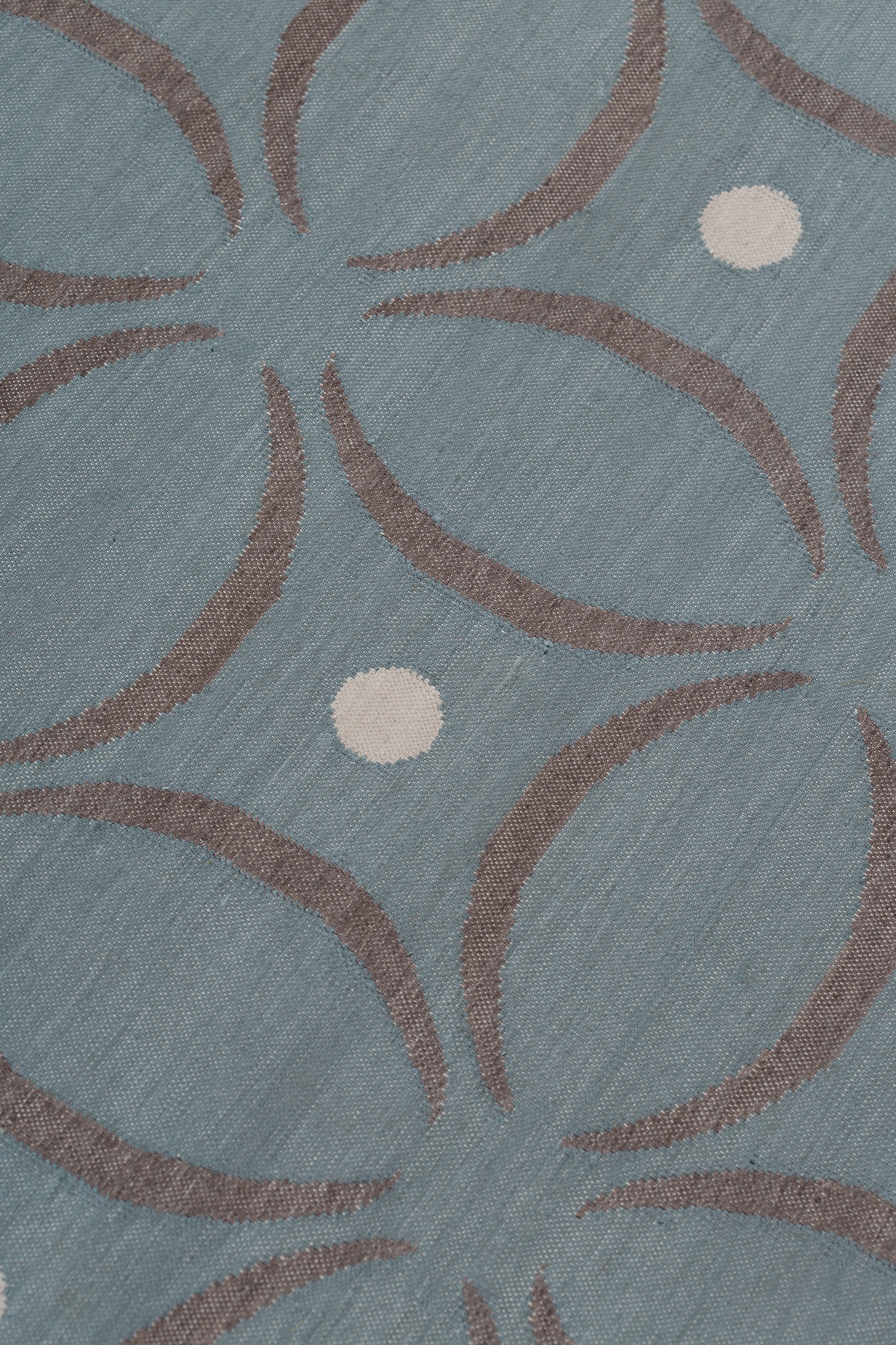 Detail of the Boe rug in Argento, featuring a pattern of curved segments in grey with white circles on a blue field. 