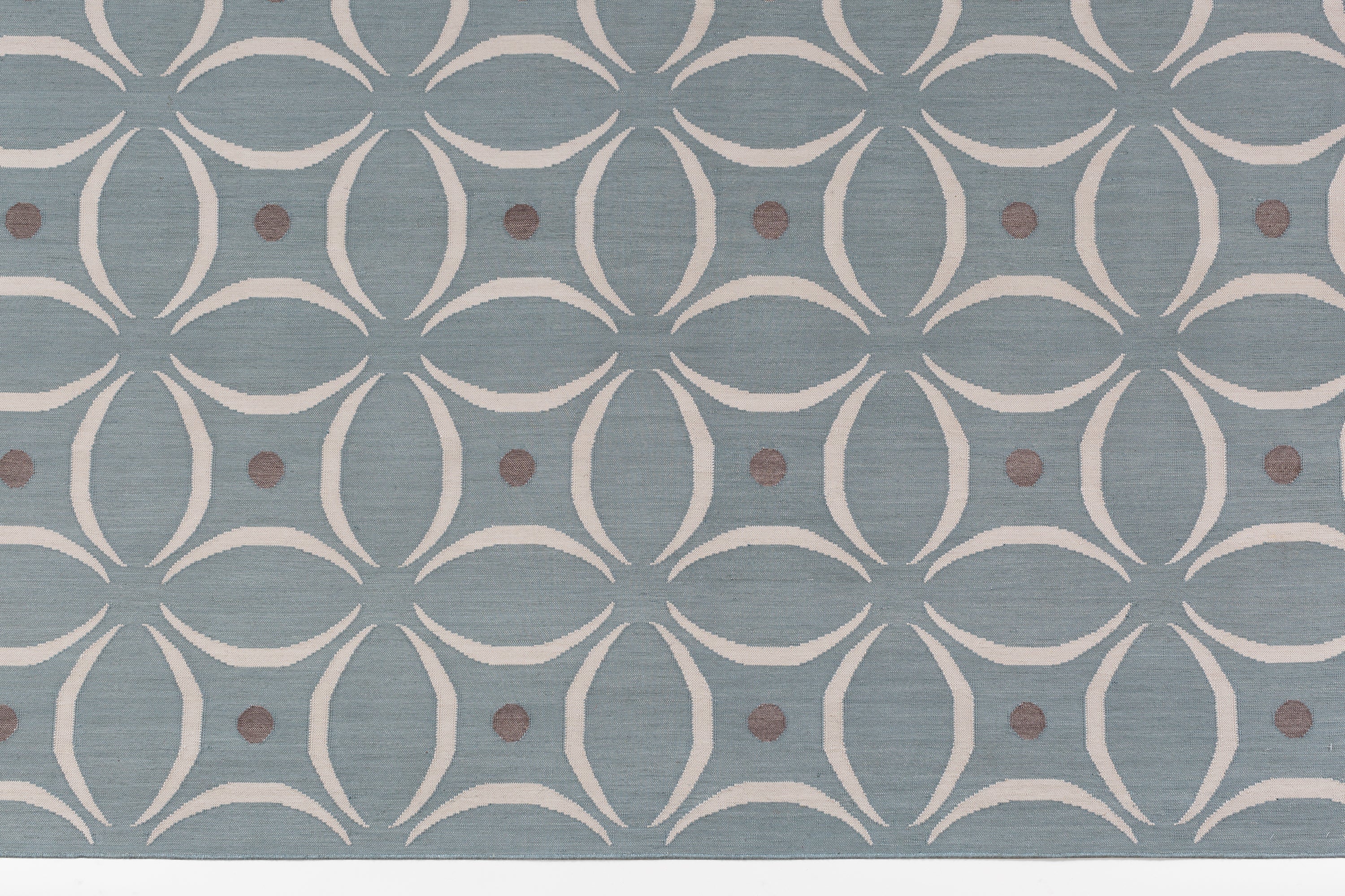 Detail of the Boe rug in Argento, featuring a pattern of white curved segments with taupe circles on a blue field. 