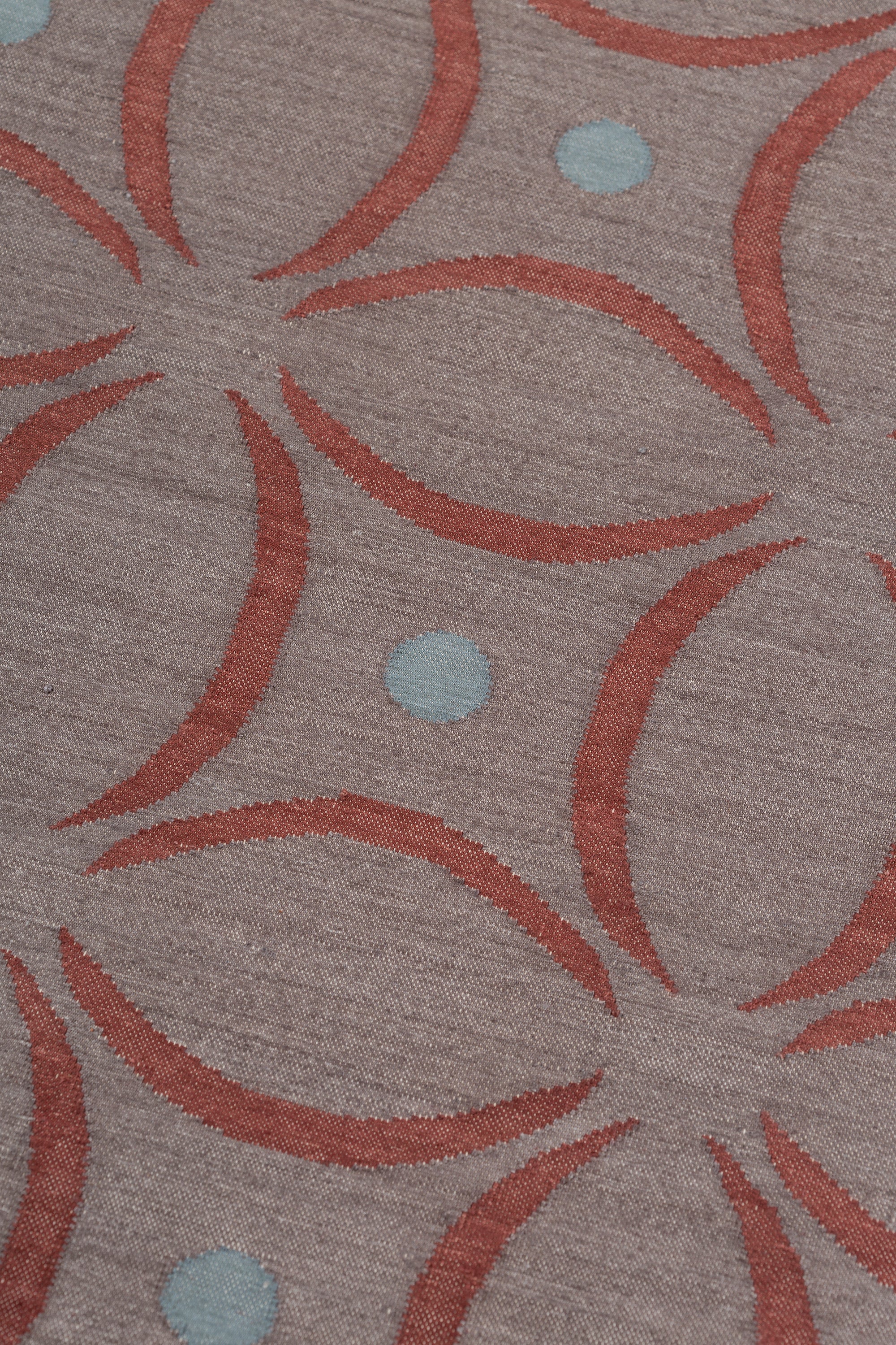Detail of the Boe rug in Tivoli, featuring a pattern of crimsoncurved segments with light blue circles on a heather purple field. 