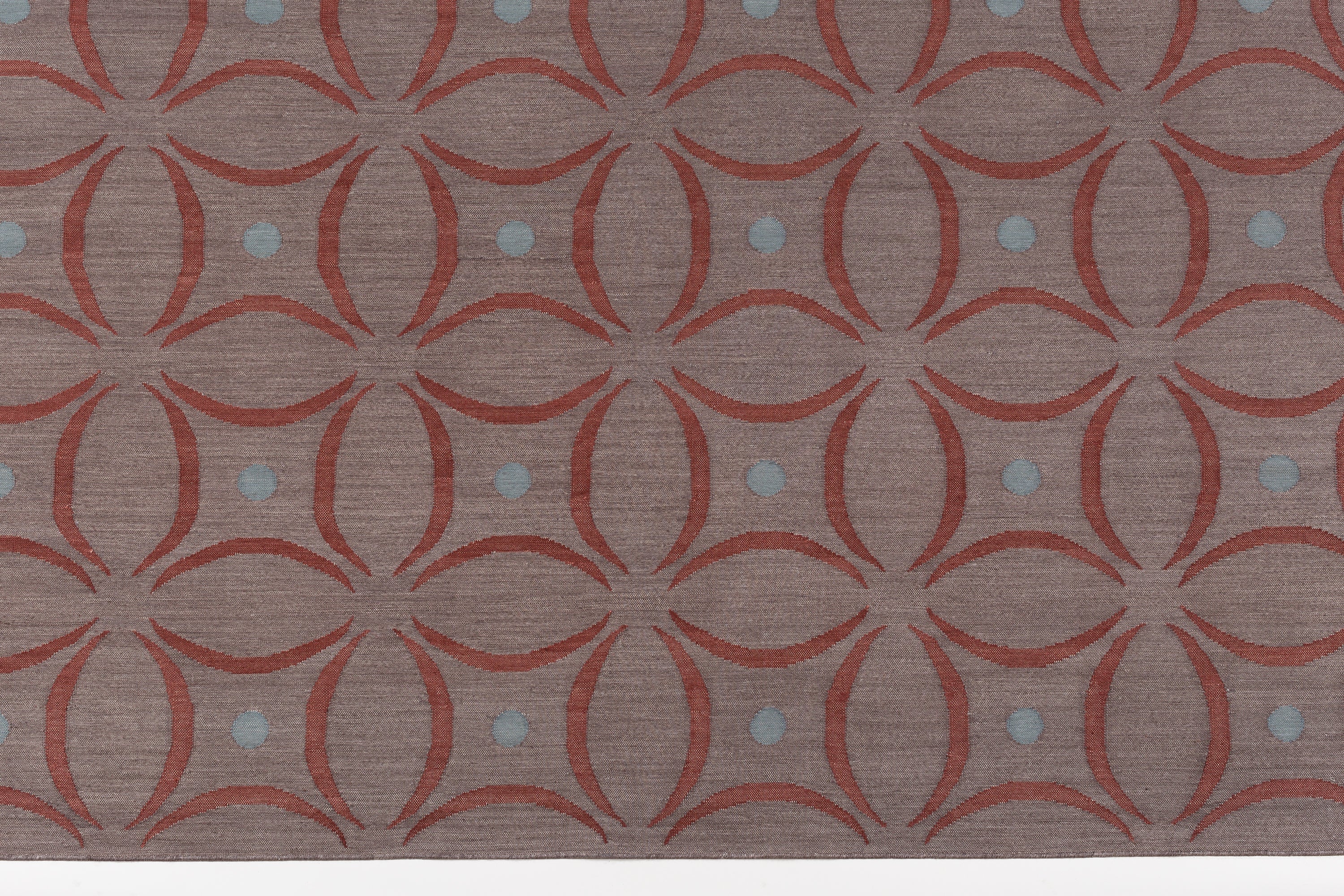 Detail of the Boe rug in Tivoli, featuring a pattern of crimsoncurved segments with light blue circles on a heather purple field. 