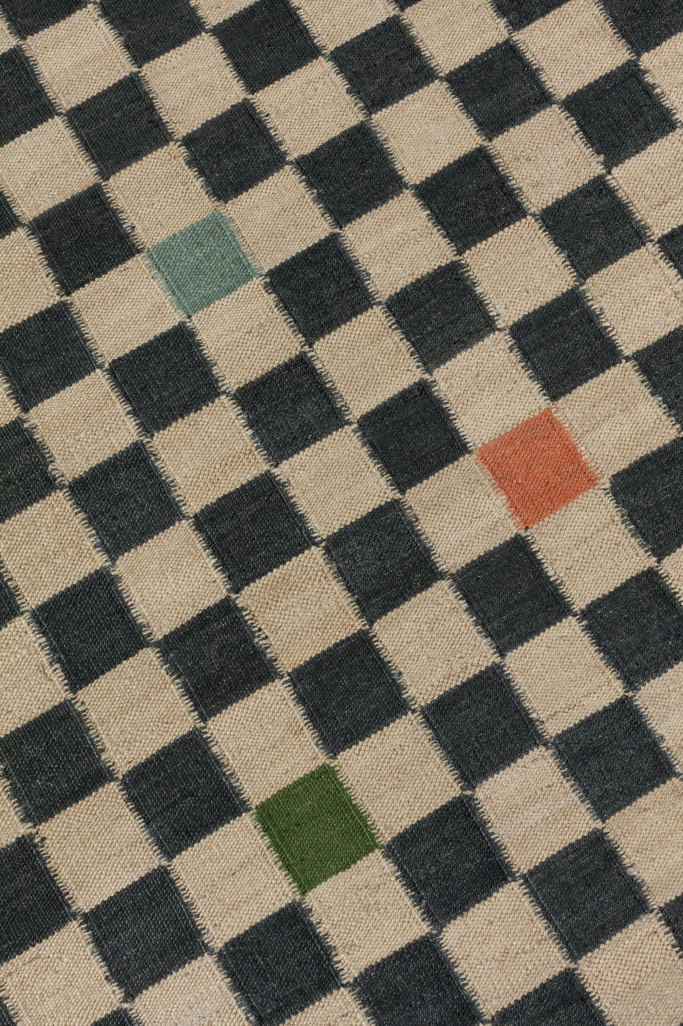 Detail of the Checkerboard Rug in King, a black and tan checkered pattern with random accents of green, sky blue and coral orange. 