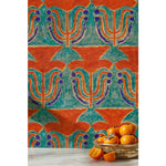 Silver bowl of persimmons in front of wallpaper with stamped painted floral motif in vibrant red and cobalt on an emerald green background, hover